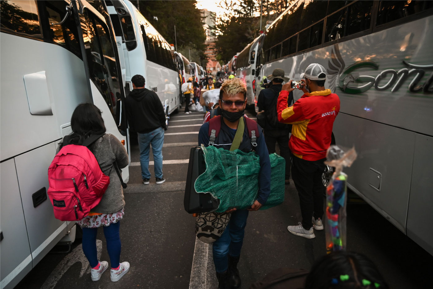 Foto de un joven Embera con sus pertenencias caminando hacia los buses para partir