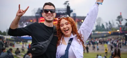 Fotografía de dos jovenes sonriendo y con las manos levantadas, de fondo desenfocado una de las tarimas del FEP y mucha gente alrededor
