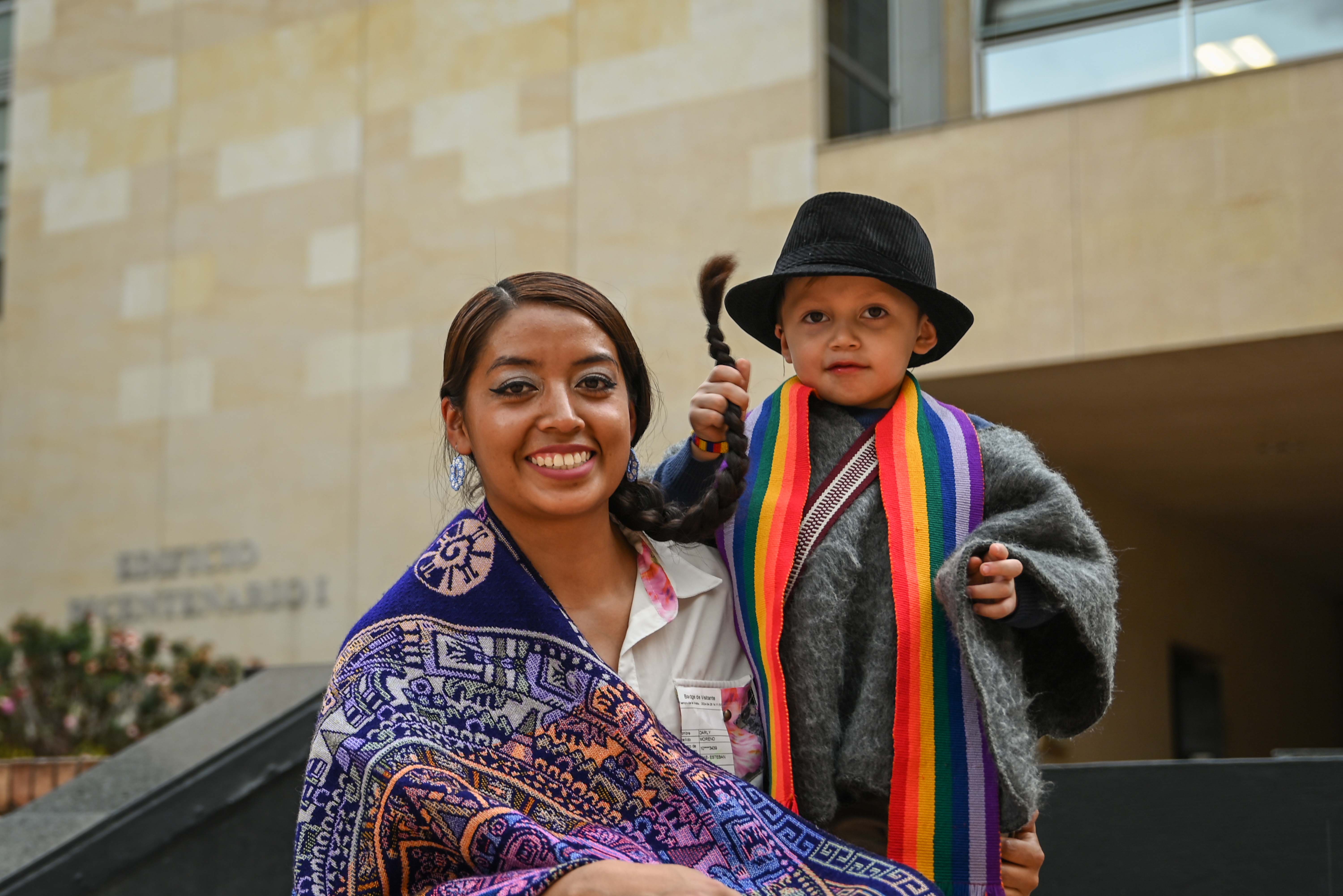 Foto de una mujer joven indígena sonriendo acompañada de su hijo de brazos 