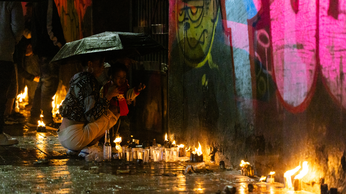 Foto de una joven mujer con su hija pequeña bajo la lluvia viendo las velas de la calle