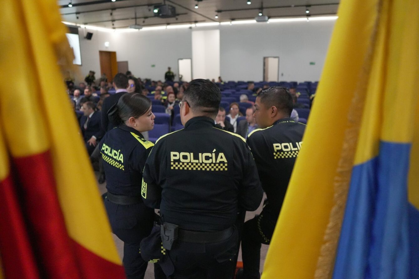 Foto donde se ven tres policias de espaldas y se identifican las banderas de Bogotá y de Colombia