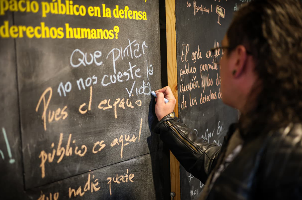Foto de una mujer escribiendo un mensaje sobre un talbero de fondo negro.