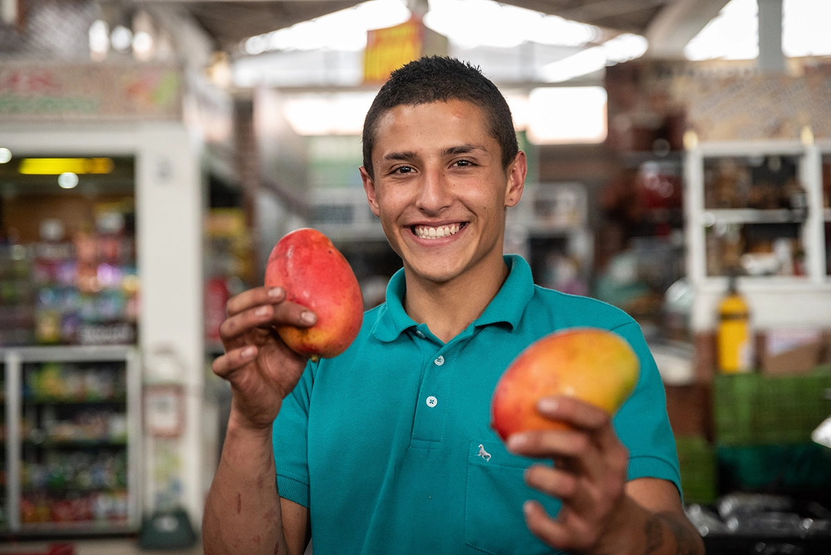 Foto de un joven sonriendo mostrando dos mangos que sostiene con sus manos.