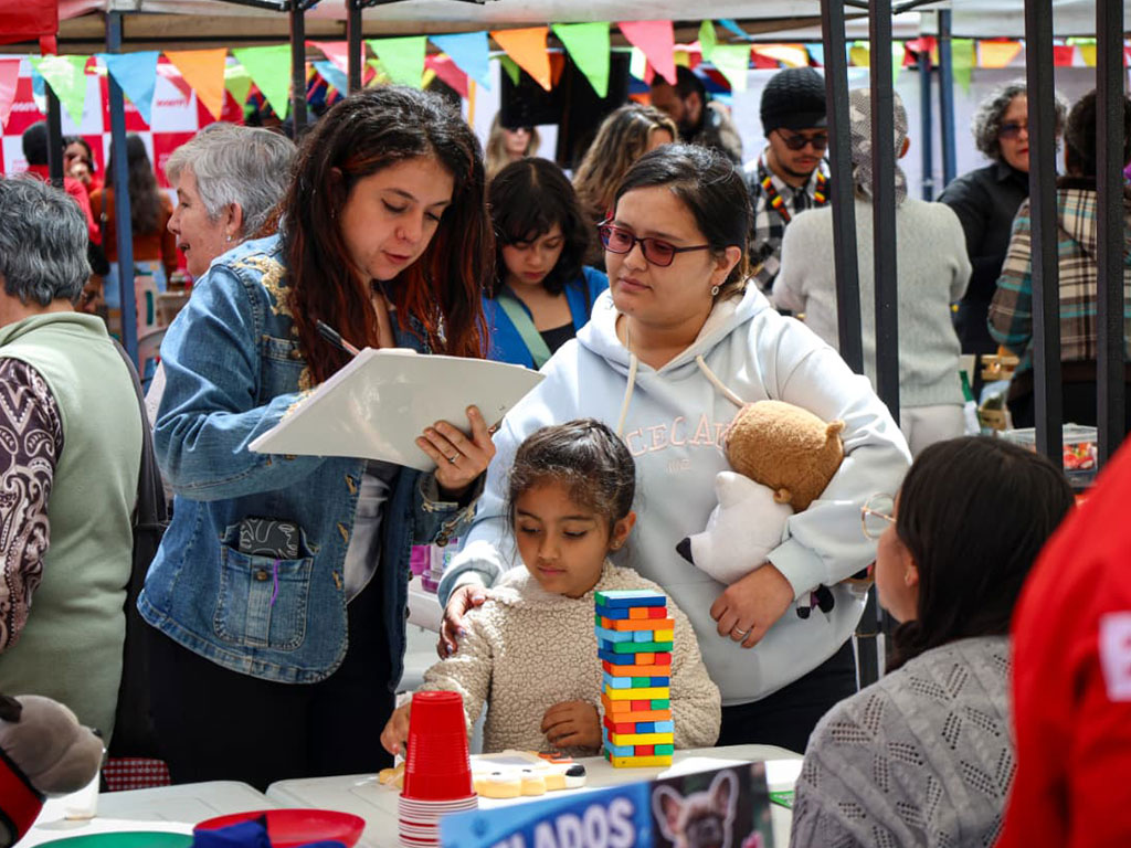 Foto de madre e hija pequeña en la feria hablando con una joven de cabello ondulado