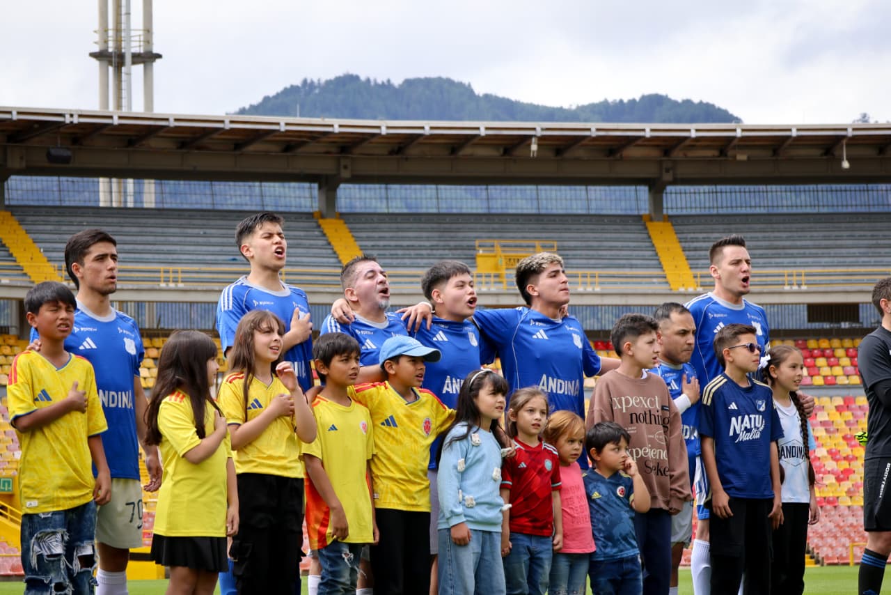 Foto de los jugadores de Millonarios formados y en frente niñas y niños con camiseta amarilla que los acompañan en la formación.