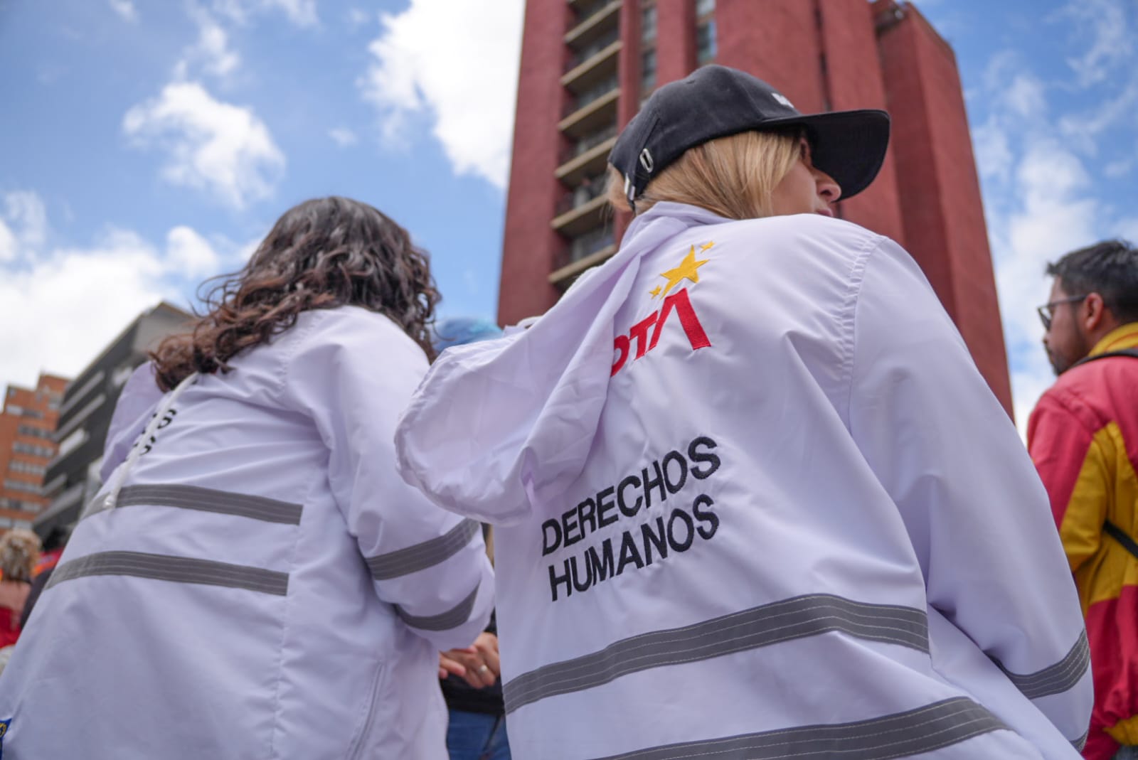 Foto de dos funcionarias de la SDG de chaqueta blanca de espaldas observando la marcha