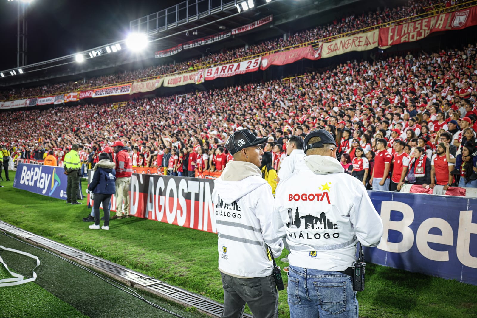 Foto de dos funcionarios de Dialogo de la SDG mirando hacia la tribuna de los hinchas de Santa Fe
