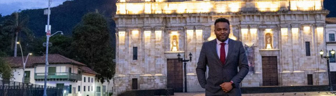 Se aprecia sonriente y de pie a Jhon Fredy Silva hombre de piel negra ubicado adelante de la Catedral Primada de Bogotá