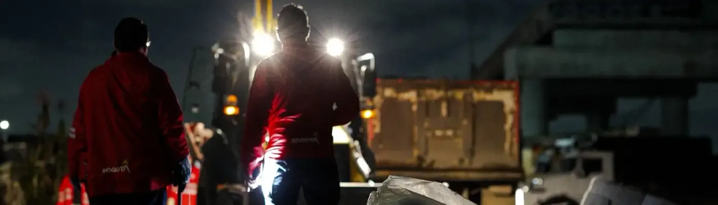 Fotografía de dos funcionarios con chaqueta roja, en la noche en operativo de recolección de escombros
