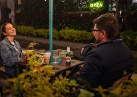 Una pareja joven mujer y hombre en la noche compartiendo una bebida y la mujer está sonriendo