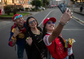 Fotografía de tres hinchas con sus camisetas de futbol felices tomandose una selfie en el barrio