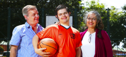 Fotografia de dos adultos hombre y mujer, en medio su hijo con sindrome de down, toso sonriendo felices.
