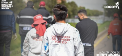 En la imagen se observan varios uniformados y gestores caminando por un corredor vial cercano a un canal, uno de ellos con chaqueta blanca que dice “Defensores del Espacio Público”.