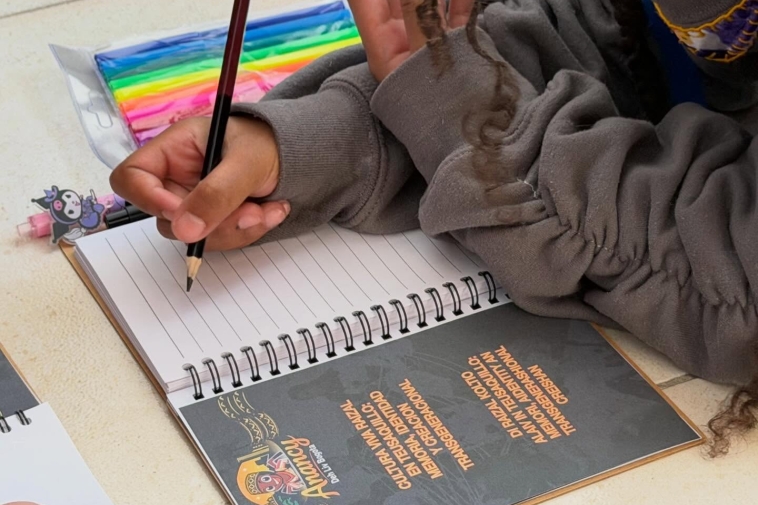 Fotografía de una mano con un lapiz escribiendo en un cuadreno
