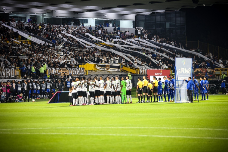Fotografía de un estadio lleno y los equipos de fútbol ordenados
