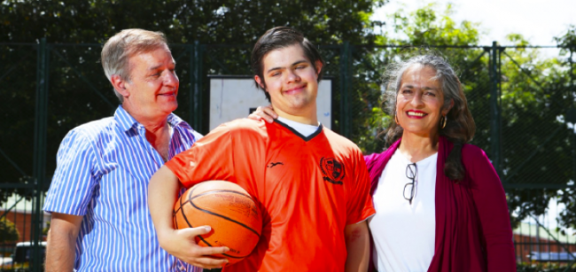 Fotografia de dos adultos hombre y mujer, en medio su hijo con sindrome de down, toso sonriendo felices.
