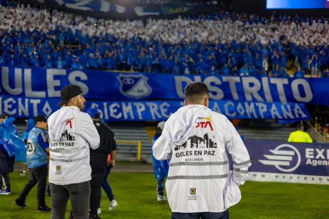 Gestores de diálogo en el estadio y de fondo la barra azul de Millonarios