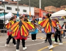 Grupo de niñas y jóvenes participa en una presentación cultural con coloridas alas de mariposa en un espacio comunitario al aire libre.