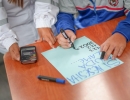 Foto donde se aprecian las manos de un menor de edad escribiendo nñumeros sobre una cartulina y a su lado se aprecian las manos de una persona adulta.