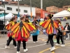 Grupo de niñas y jóvenes participa en una presentación cultural con coloridas alas de mariposa en un espacio comunitario al aire libre.